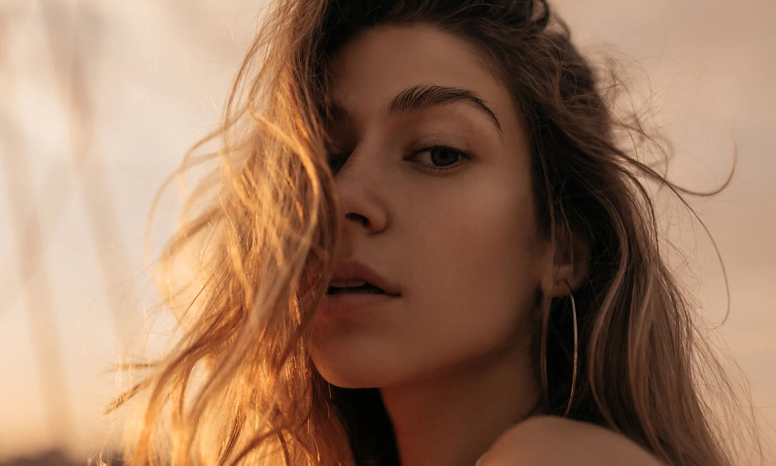 A close-up of a young woman with golden highlights in her tousled hair, gazing intently at the camera in natural light - Chin Implant in West Hollywood, CA