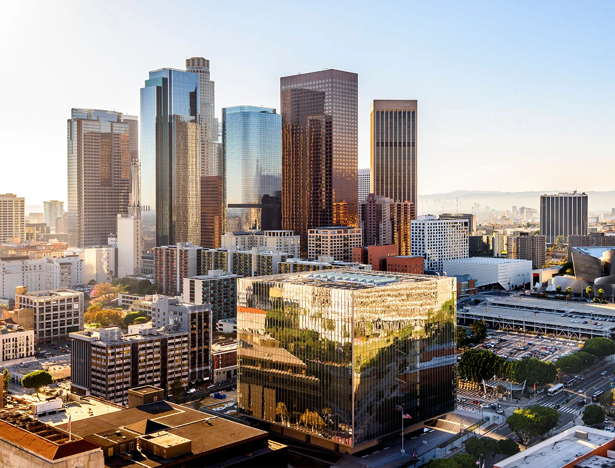 A panoramic view of downtown Los Angeles, showcasing sleek skyscrapers and a modern reflective building under a clear sky. - Out of Town in West Hollywood, CA