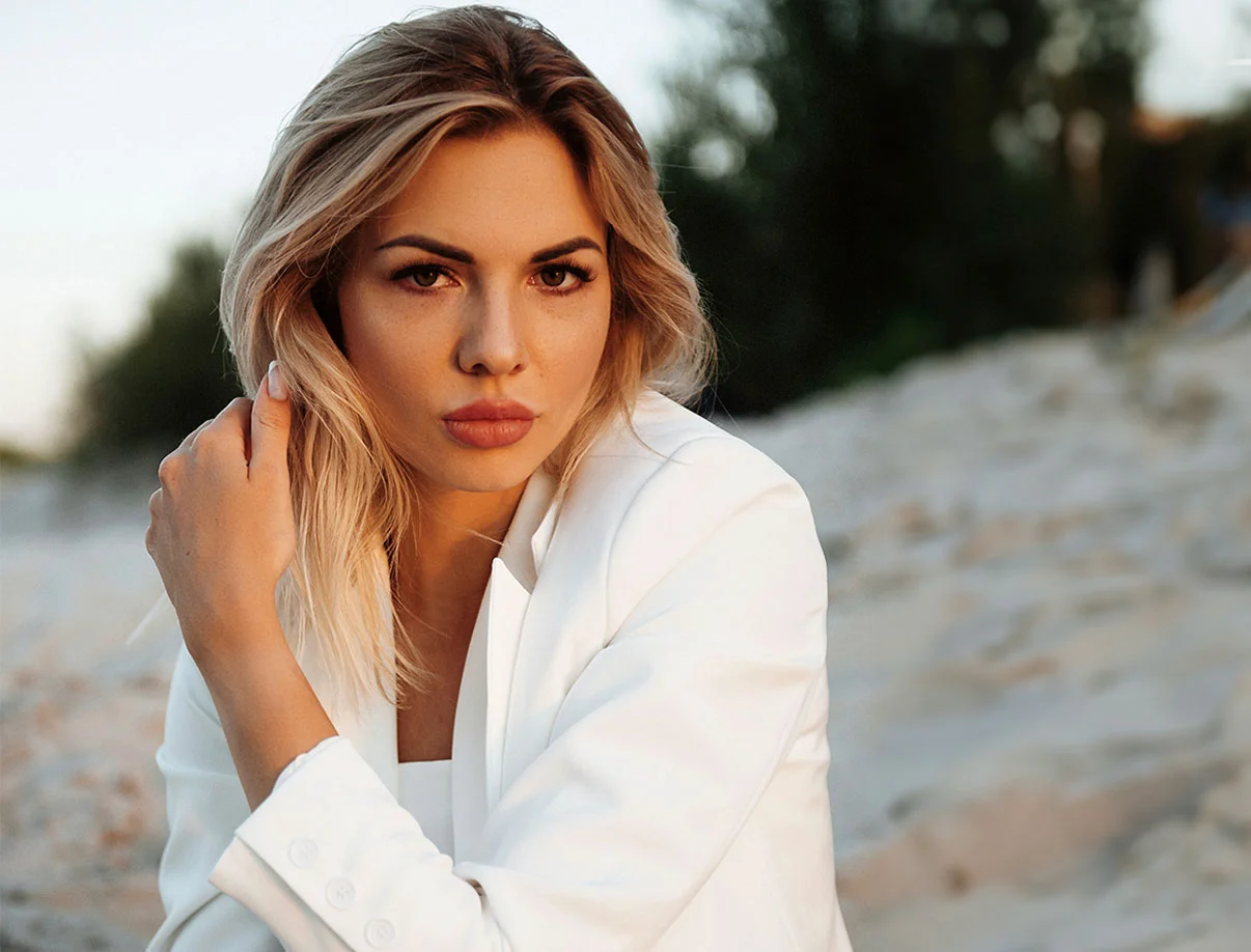 A blonde woman in a white blazer sitting on a beach at sunset, showcasing effortless beauty and tranquility - Stelar Longevity in West Hollywood, CA