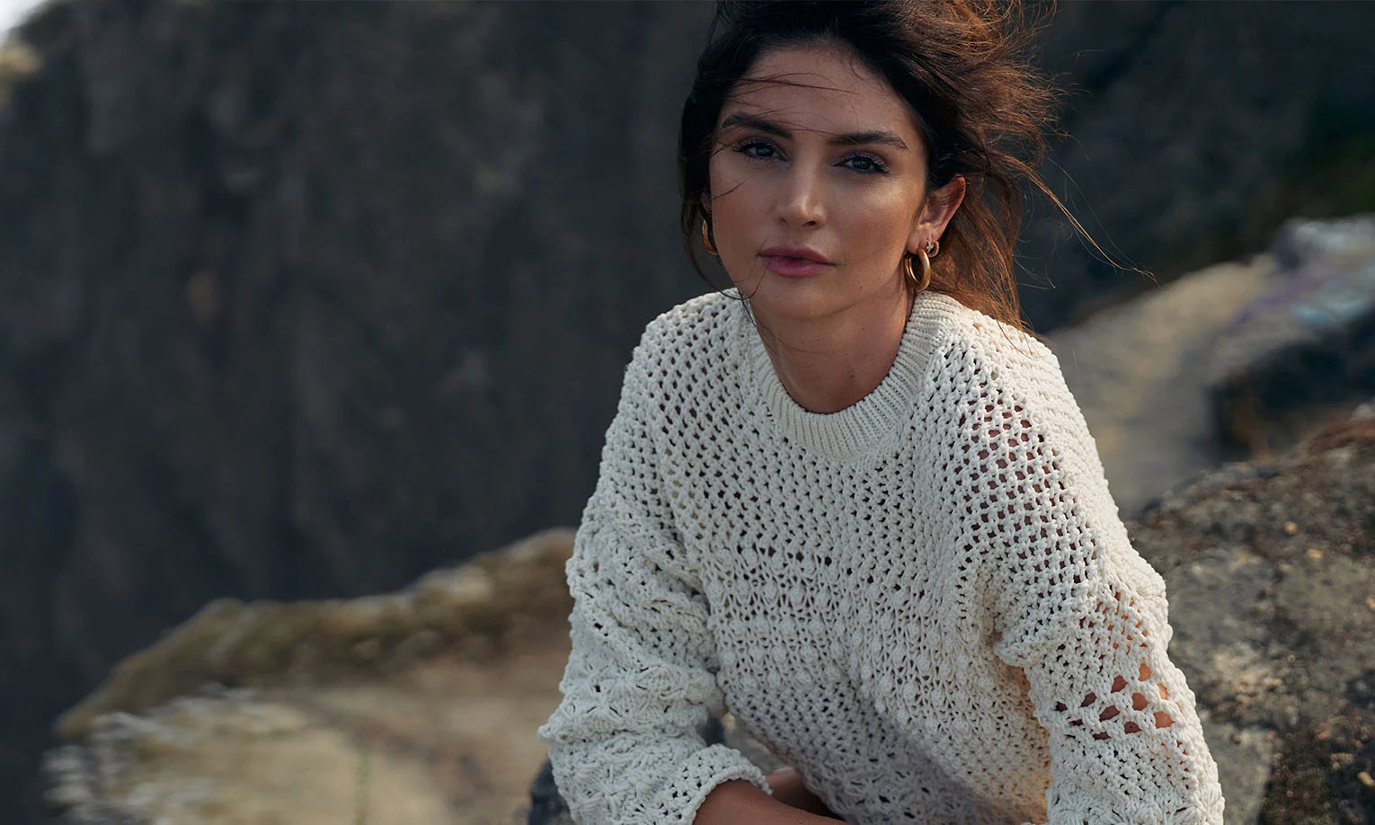 A woman wearing a knitted sweater, sitting outdoors against a rocky backdrop, embodying natural beauty and simplicity - Stelar Longevity in West Hollywood, CA