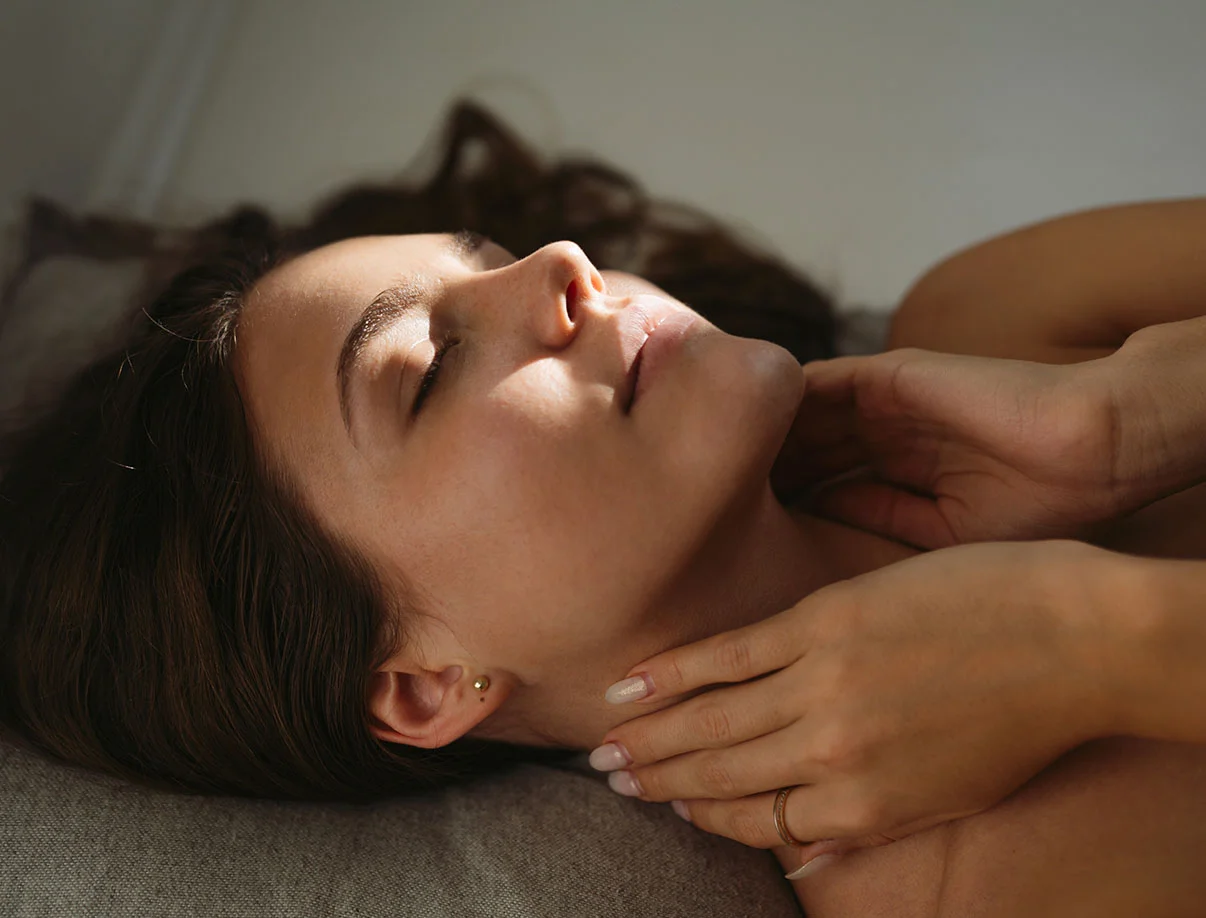 A serene woman with long hair lies on a pillow, gently touching her neck, basking in soft natural light. - Sun and Brown Spot Removal in West Hollywood, CA