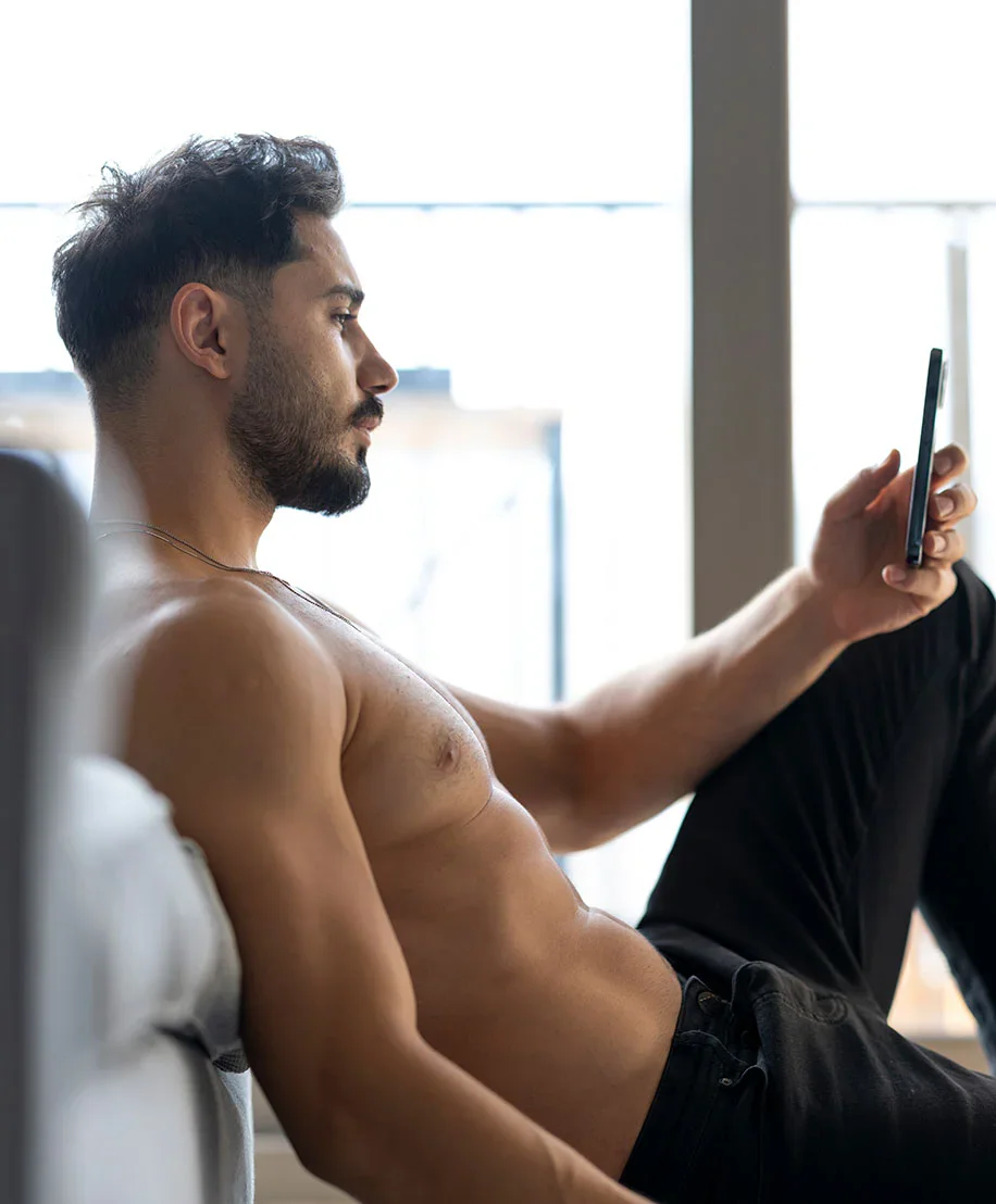 Why choose Dr. Motykie for your Gynecomastia procedure in Beverly Hills? Middle aged male with no shirt scrolling on social media.